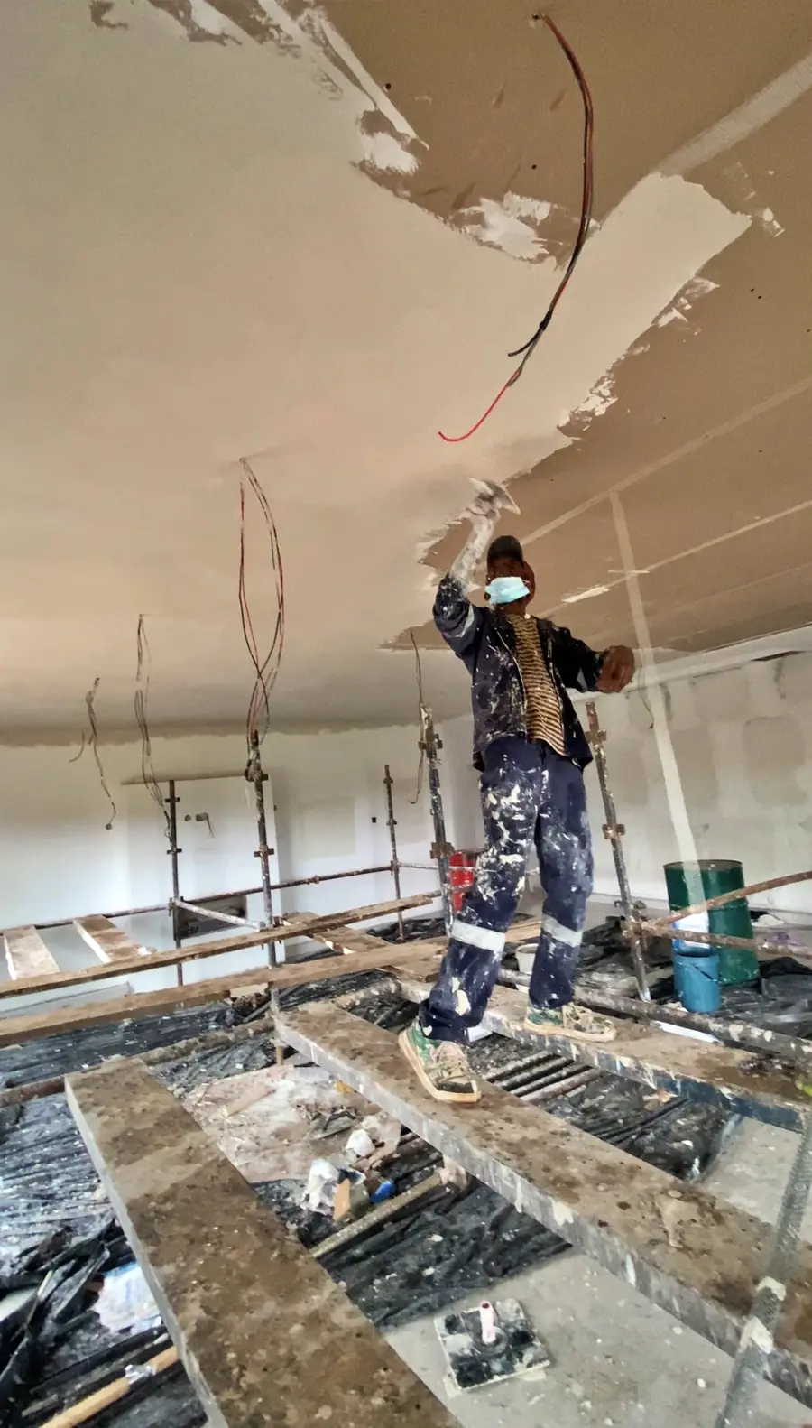 Tawaka Contracting plasterer skimming a new ceiling from staging boards in Gletwin, Harare, with electrical cabling still