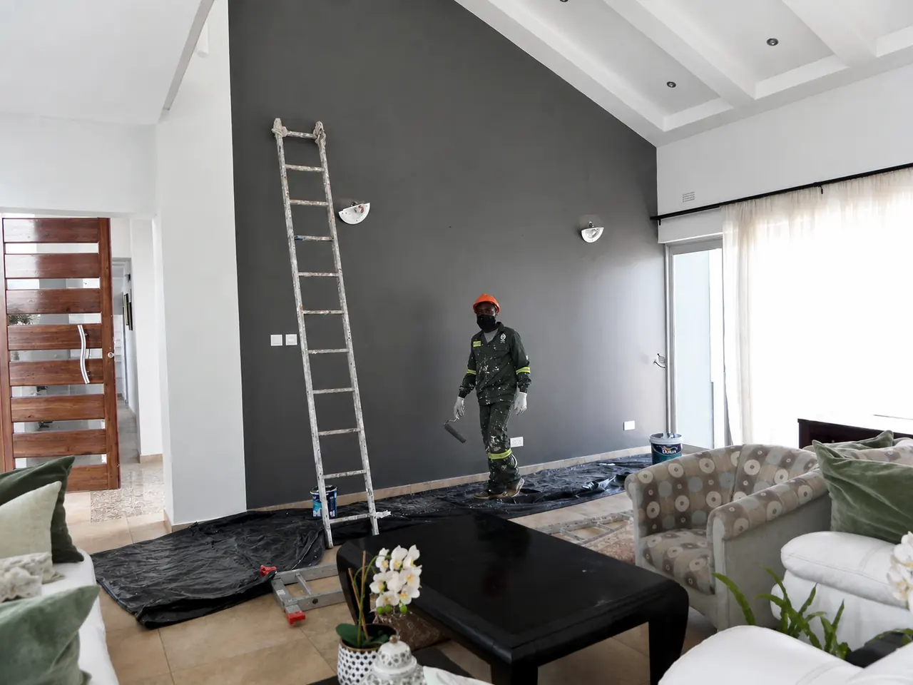 Interior painting contractor Harare — Tawaka Contracting painter applying a charcoal feature wall in an occupied Chisipite living room