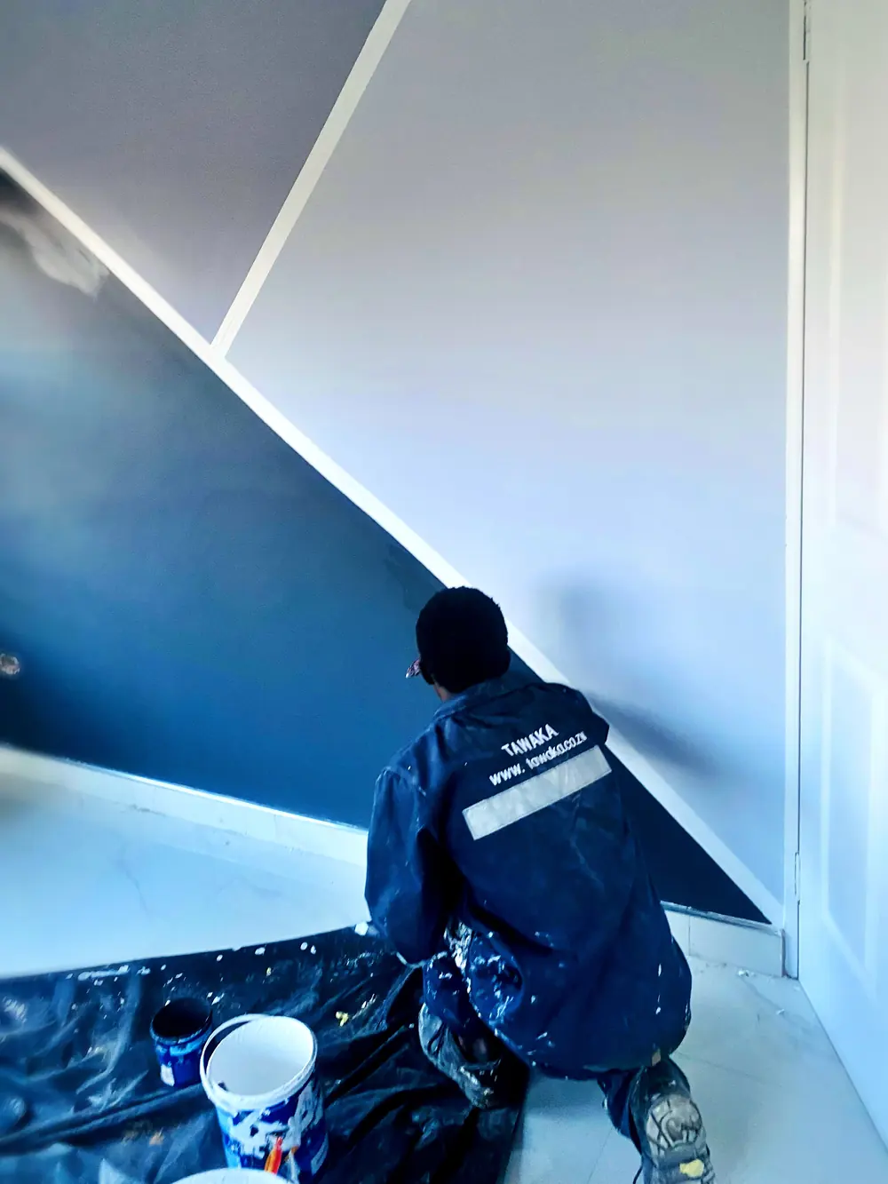 Painting contractor Harare — Tawaka Contracting painter cutting a crisp diagonal two-tone feature wall in navy and grey