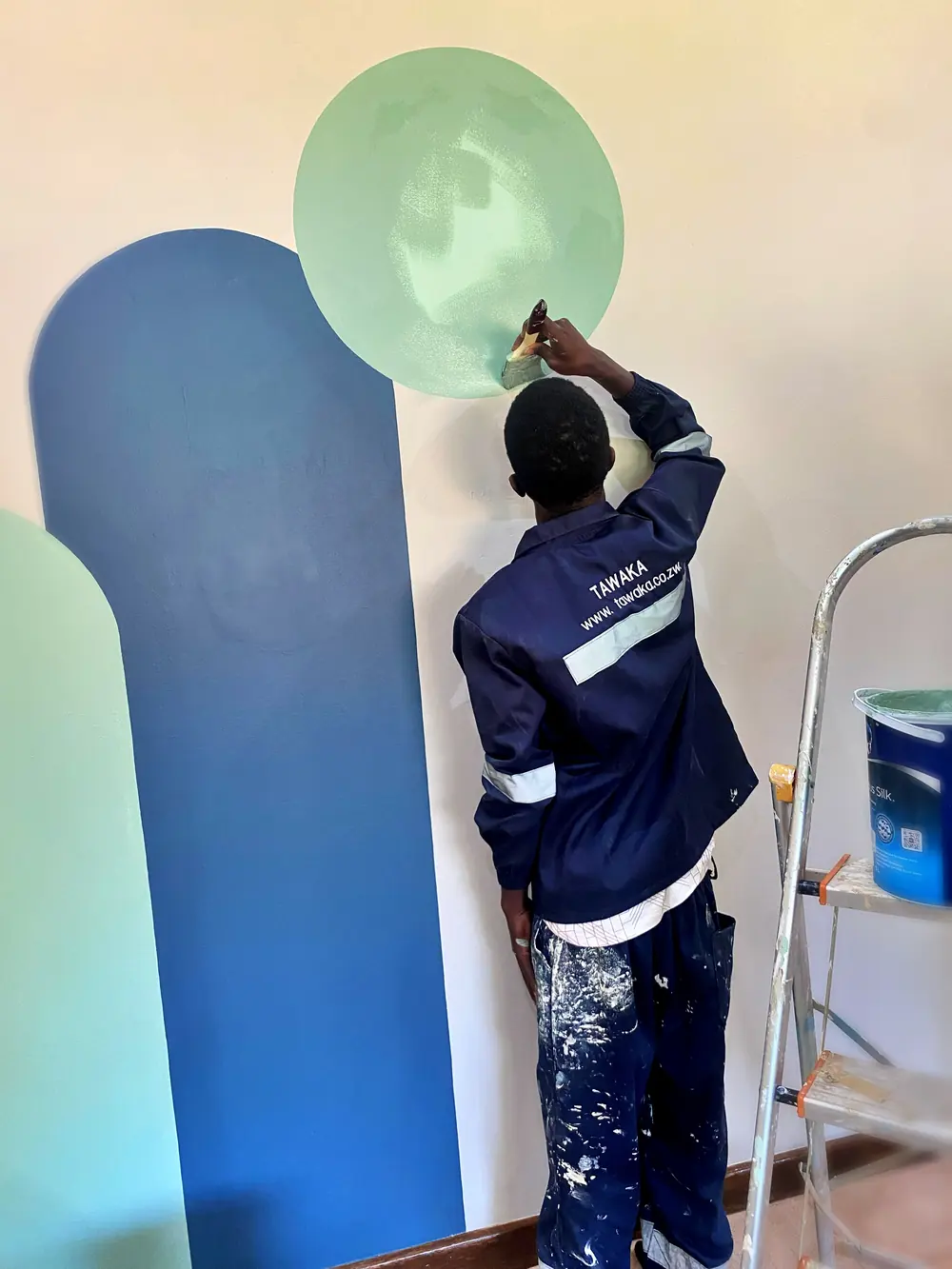 Tawaka Contracting painter applying shaped colour blocks to a pre-school classroom wall at Grange, Zimbabwe