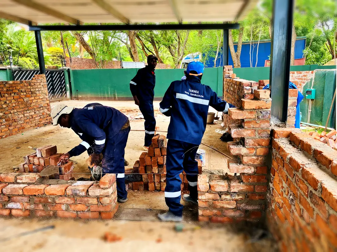 Tawaka Contracting bricklaying team raising face-brick walls under a steel canopy in Highlands, Zimbabwe
