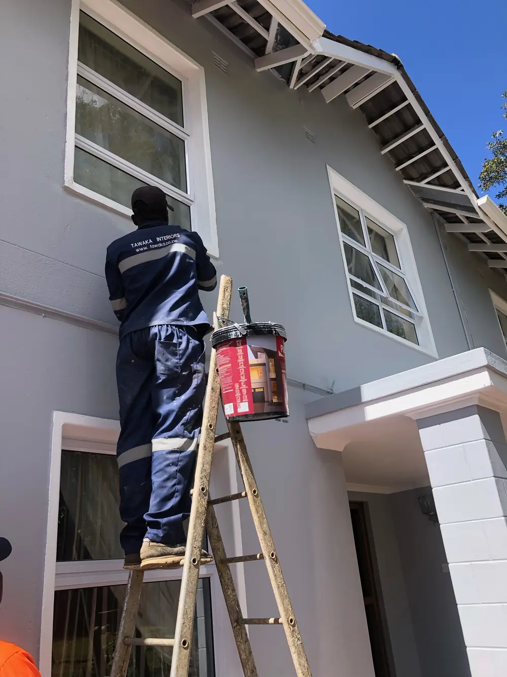 Painting contractor Harare — Tawaka Contracting painter in branded workwear cutting in exterior trim on a home in Highlands, Zimbabwe