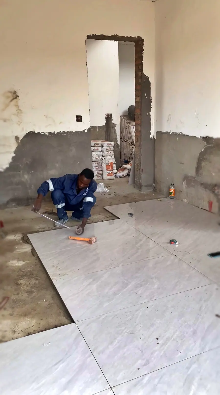 Tawaka Contracting tiler laying marble-effect floor tiles across a stripped room in Vainona, Harare