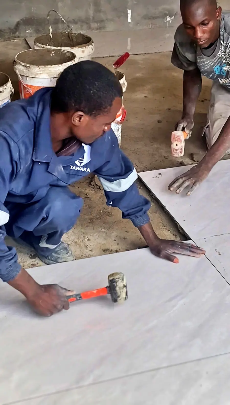 Tawaka Contracting tiler bedding a large-format floor tile with a rubber mallet on a site in Vainona, Harare