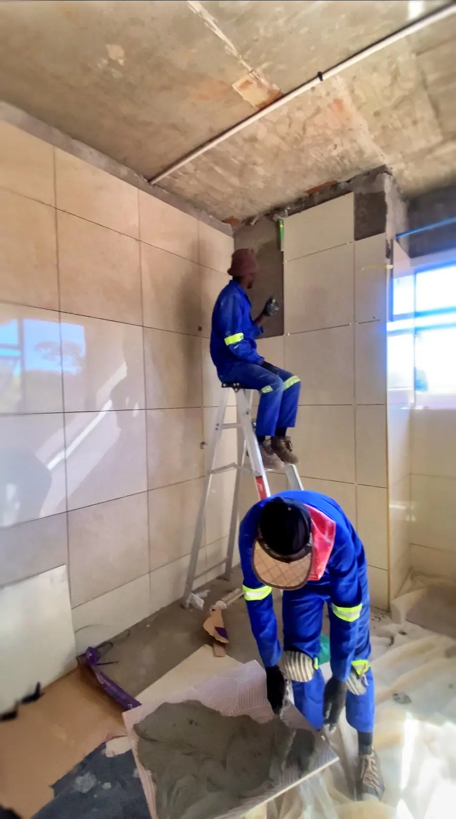 Two Tawaka Contracting tilers fixing large-format wall tiles from a ladder during a renovation in Glen Lorne, Harare